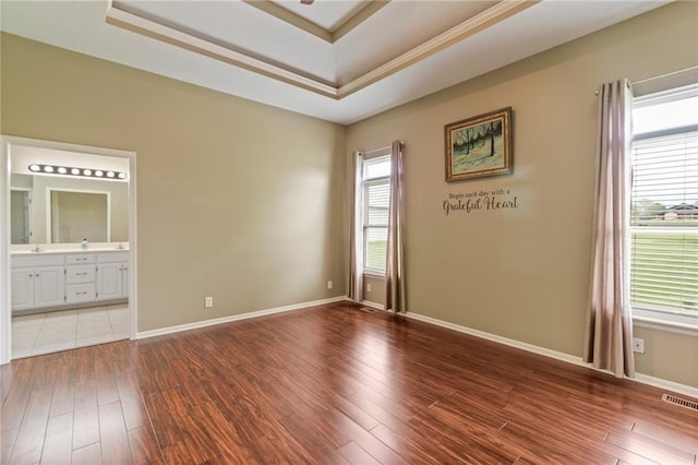 unfurnished room featuring visible vents, wood finished floors, a tray ceiling, and a wealth of natural light