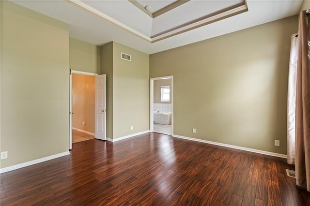 empty room featuring visible vents, wood finished floors, baseboards, a high ceiling, and a tray ceiling