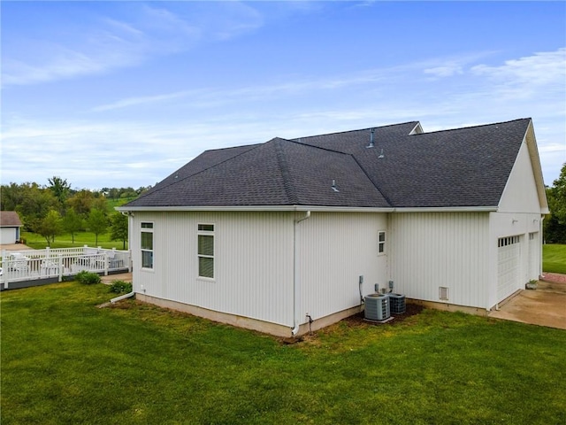 rear view of property with an attached garage, roof with shingles, a yard, and concrete driveway