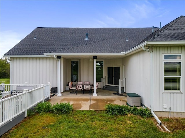 back of property with a lawn, a shingled roof, and a patio area