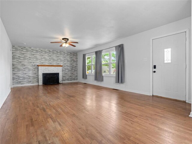 unfurnished living room with visible vents, wood finished floors, baseboards, ceiling fan, and a tiled fireplace