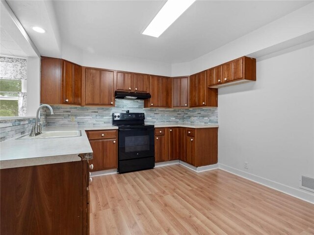 kitchen with brown cabinetry, a sink, light countertops, under cabinet range hood, and black range with electric cooktop