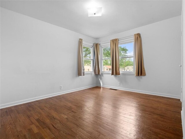 unfurnished room with visible vents, dark wood-style flooring, and baseboards