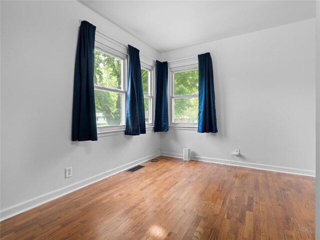 spare room with baseboards, visible vents, a healthy amount of sunlight, and wood finished floors
