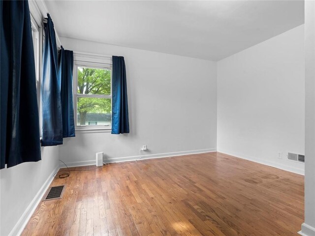 unfurnished room with visible vents, baseboards, and hardwood / wood-style flooring
