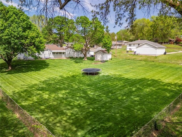 view of yard with an outdoor structure, a fenced backyard, a shed, a trampoline, and a residential view