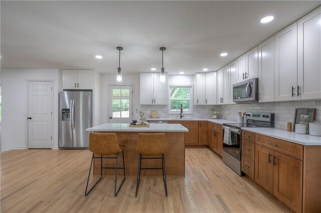 kitchen with a sink, a kitchen breakfast bar, a center island, stainless steel appliances, and light wood-type flooring