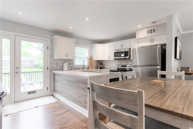 kitchen featuring visible vents, decorative backsplash, white cabinetry, light wood finished floors, and stainless steel appliances