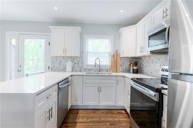 kitchen featuring decorative backsplash, dark wood-style flooring, a peninsula, a sink, and stainless steel appliances