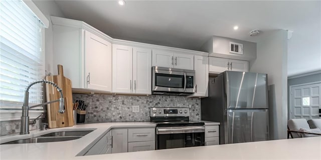 kitchen with white cabinets, appliances with stainless steel finishes, a sink, light countertops, and decorative backsplash