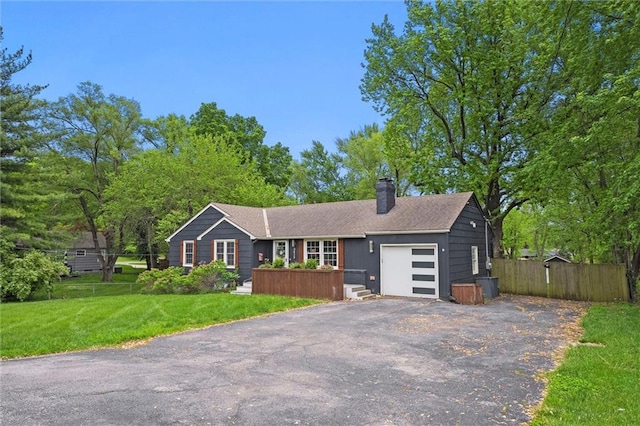 ranch-style house featuring driveway, a chimney, a front yard, fence, and an attached garage