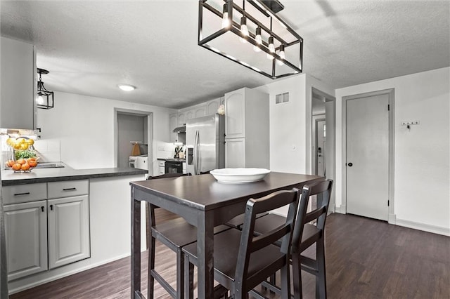 kitchen featuring stainless steel refrigerator with ice dispenser, a textured ceiling, visible vents, and dark countertops