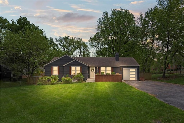 ranch-style home featuring a chimney, a lawn, a garage, fence, and aphalt driveway