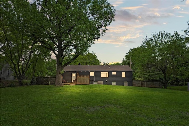 back of house at dusk featuring fence and a lawn