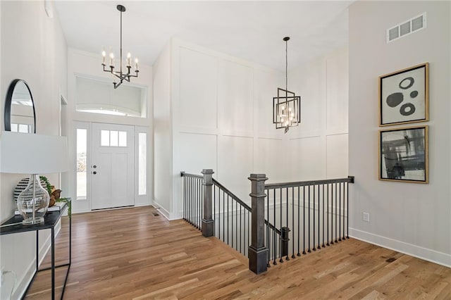 entryway with a notable chandelier, baseboards, light wood finished floors, visible vents, and a towering ceiling
