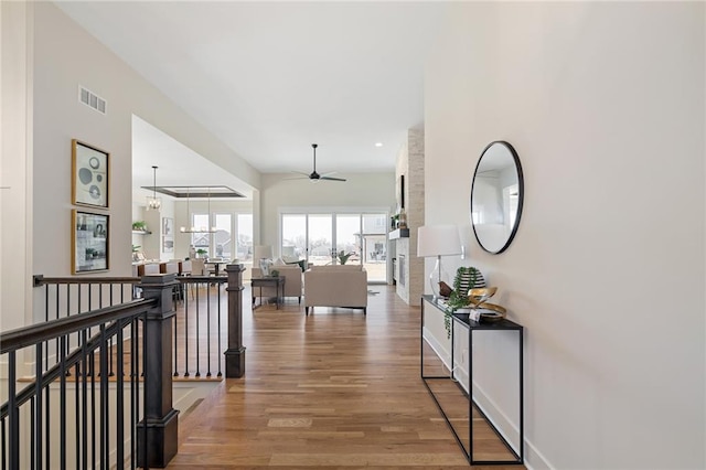 corridor featuring wood finished floors, visible vents, an upstairs landing, and baseboards