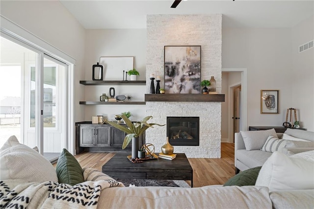 living area featuring a stone fireplace, visible vents, and wood finished floors
