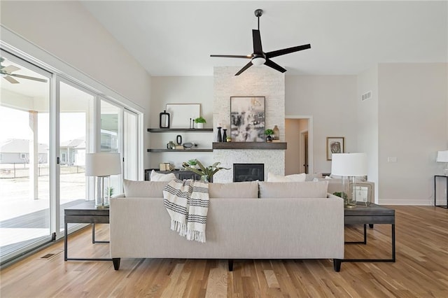 living room with ceiling fan, a stone fireplace, visible vents, and wood finished floors