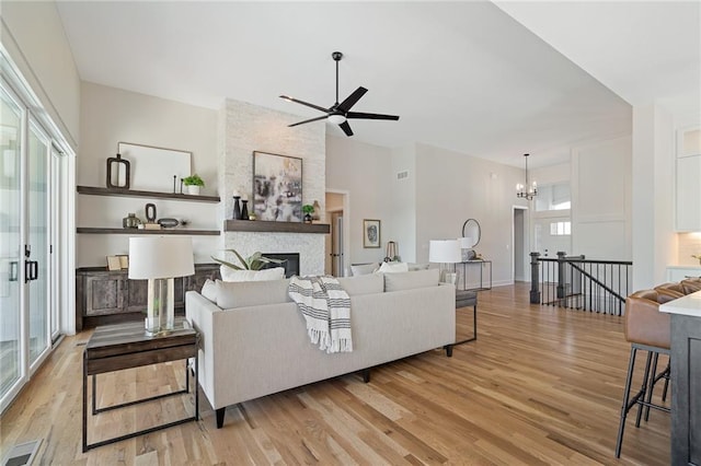 living room featuring light wood finished floors, a stone fireplace, a ceiling fan, and visible vents