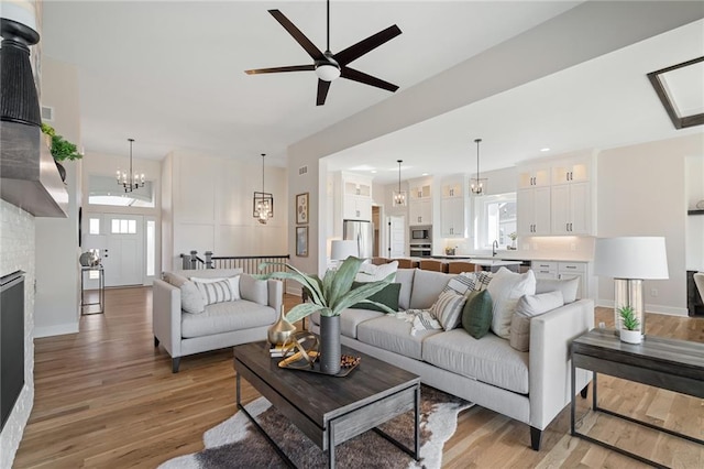living room with baseboards, light wood-style floors, visible vents, and ceiling fan with notable chandelier