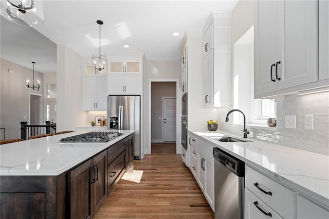 kitchen with a sink, a chandelier, decorative backsplash, light wood-style floors, and appliances with stainless steel finishes
