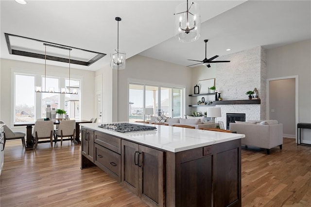 kitchen with a wealth of natural light, stainless steel gas stovetop, light wood-style flooring, and ceiling fan with notable chandelier