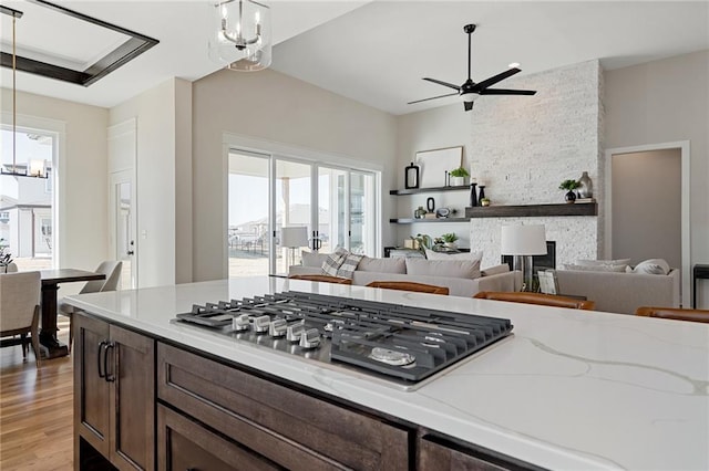 kitchen featuring decorative light fixtures, light stone countertops, ceiling fan with notable chandelier, and stainless steel gas cooktop