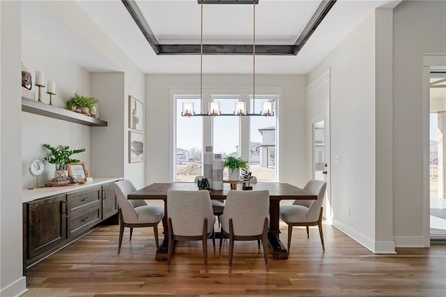 dining room featuring a tray ceiling, a chandelier, baseboards, and wood finished floors