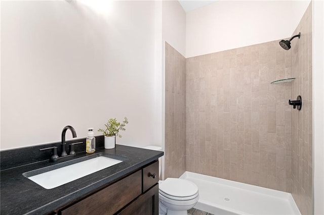 bathroom with toilet, tiled shower, and vanity