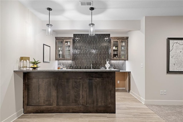 bar with decorative light fixtures, baseboards, light wood finished floors, visible vents, and indoor wet bar