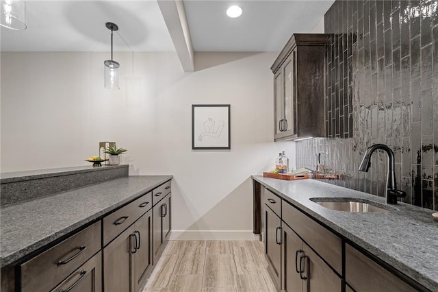 bar featuring baseboards, hanging light fixtures, a sink, tasteful backsplash, and light wood-type flooring