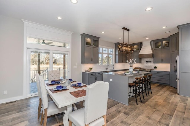 kitchen with wood finished floors, recessed lighting, backsplash, a center island, and custom range hood