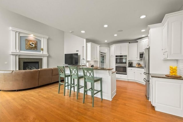 2704 SW Gray Ln, Lees Summit, MO 64081 - kitchen featuring open floor plan, light wood-style floors, tasteful backsplash, a kitchen breakfast bar, and white cabinets