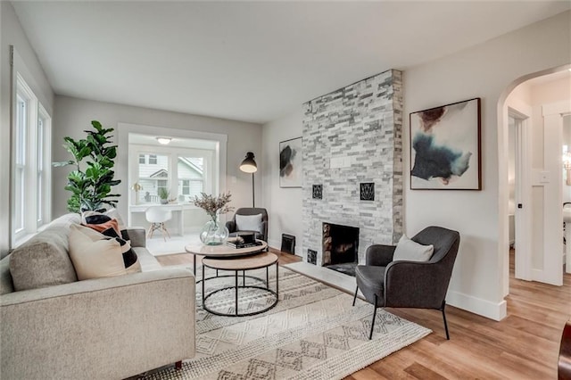 living room with wood finished floors, arched walkways, a stone fireplace, and baseboards
