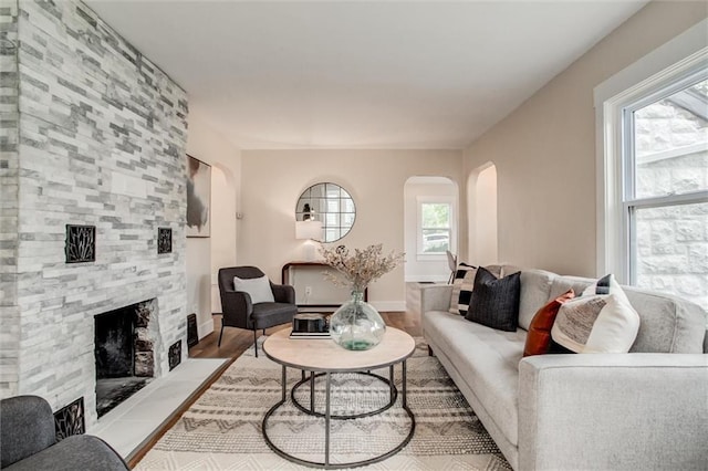 living area with arched walkways, a fireplace, healthy amount of natural light, and wood finished floors