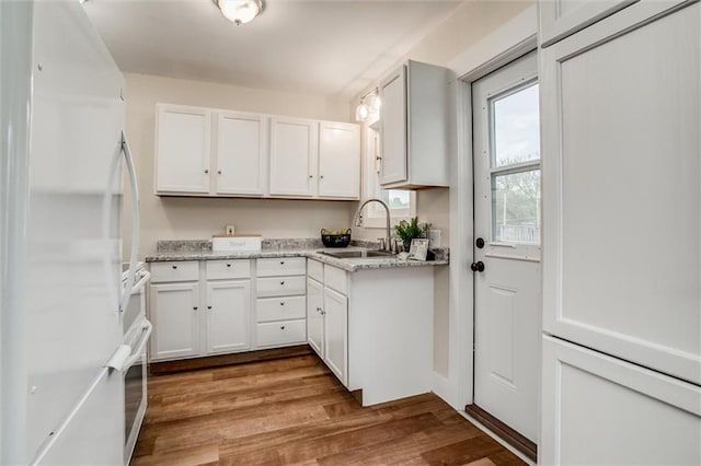 kitchen featuring freestanding refrigerator, a sink, white cabinetry, and wood finished floors