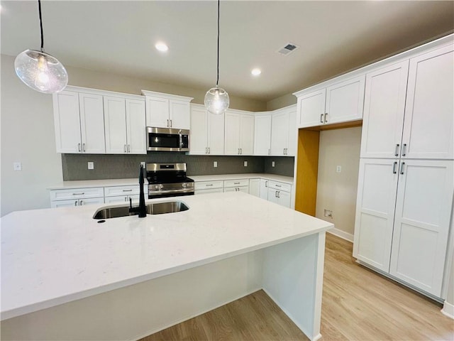 kitchen featuring a sink, appliances with stainless steel finishes, light wood finished floors, and white cabinetry