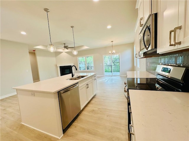 kitchen featuring light wood-style floors, a center island with sink, white cabinets, a sink, and stainless steel appliances