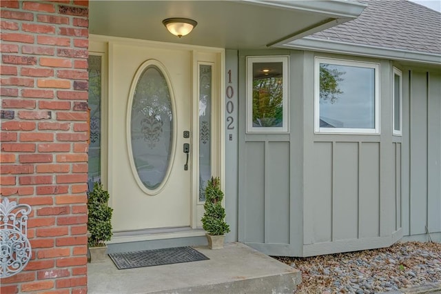 property entrance with board and batten siding, brick siding, and roof with shingles