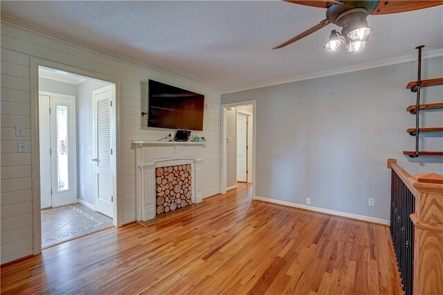 unfurnished living room featuring a ceiling fan, a fireplace, wood finished floors, baseboards, and ornamental molding