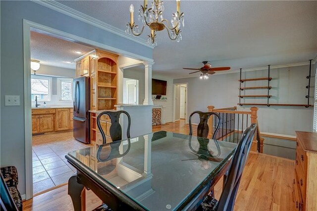 dining space with ornamental molding, decorative columns, light wood-type flooring, a textured ceiling, and ceiling fan with notable chandelier