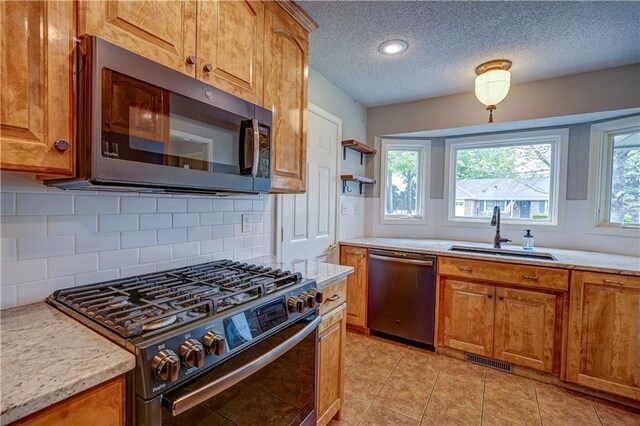 kitchen featuring brown cabinetry, a sink, backsplash, and stainless steel appliances