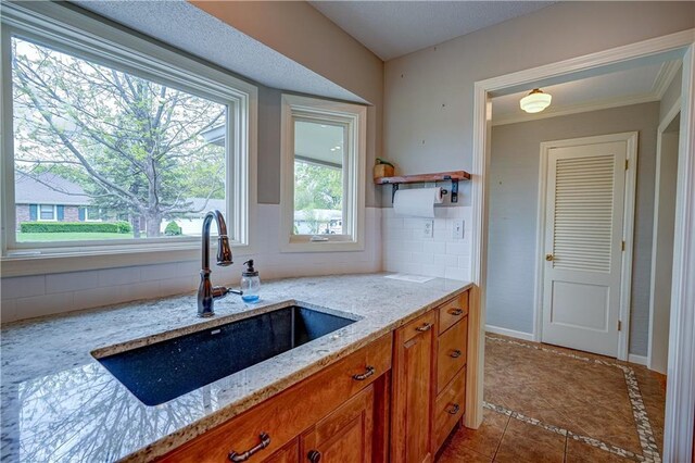 kitchen with brown cabinets, backsplash, tile patterned floors, and a sink