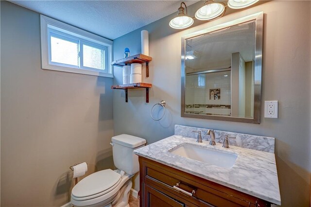 bathroom with vanity, toilet, a textured ceiling, baseboards, and a shower with door