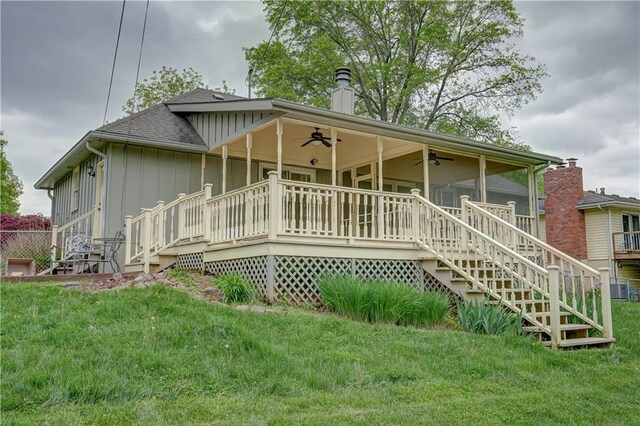 back of house featuring a shingled roof, board and batten siding, ceiling fan, stairway, and a lawn