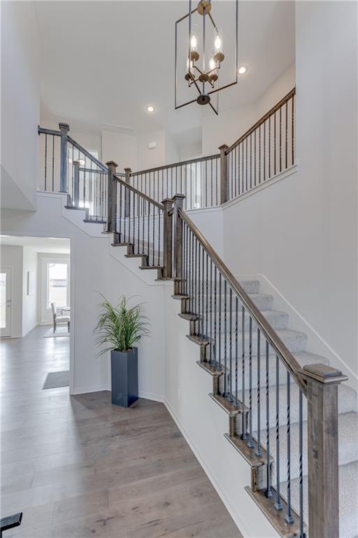 staircase featuring a towering ceiling, recessed lighting, wood finished floors, and a notable chandelier