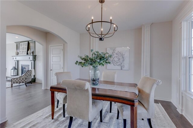 dining space with arched walkways, a large fireplace, wood finished floors, baseboards, and a notable chandelier