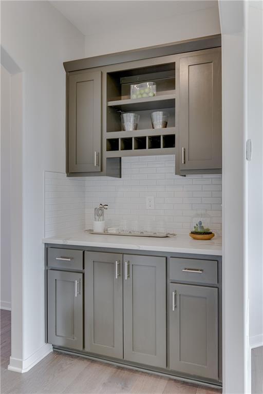 bar featuring baseboards, light wood-type flooring, and tasteful backsplash