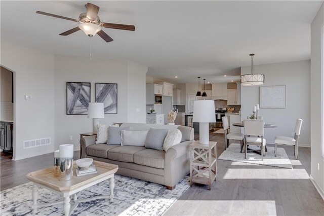 living area with ceiling fan, visible vents, wood finished floors, baseboards, and recessed lighting