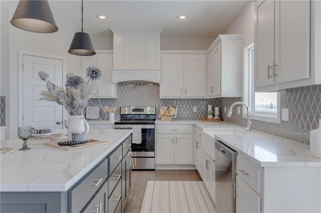 kitchen with white cabinets, light stone countertops, gray cabinets, light wood-style flooring, and stainless steel appliances